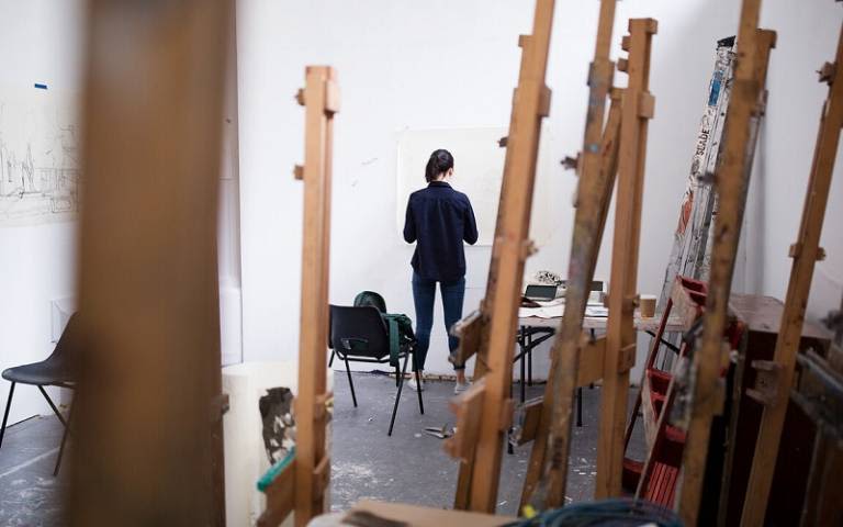 An artist surrounded by prints and wooden palettes.