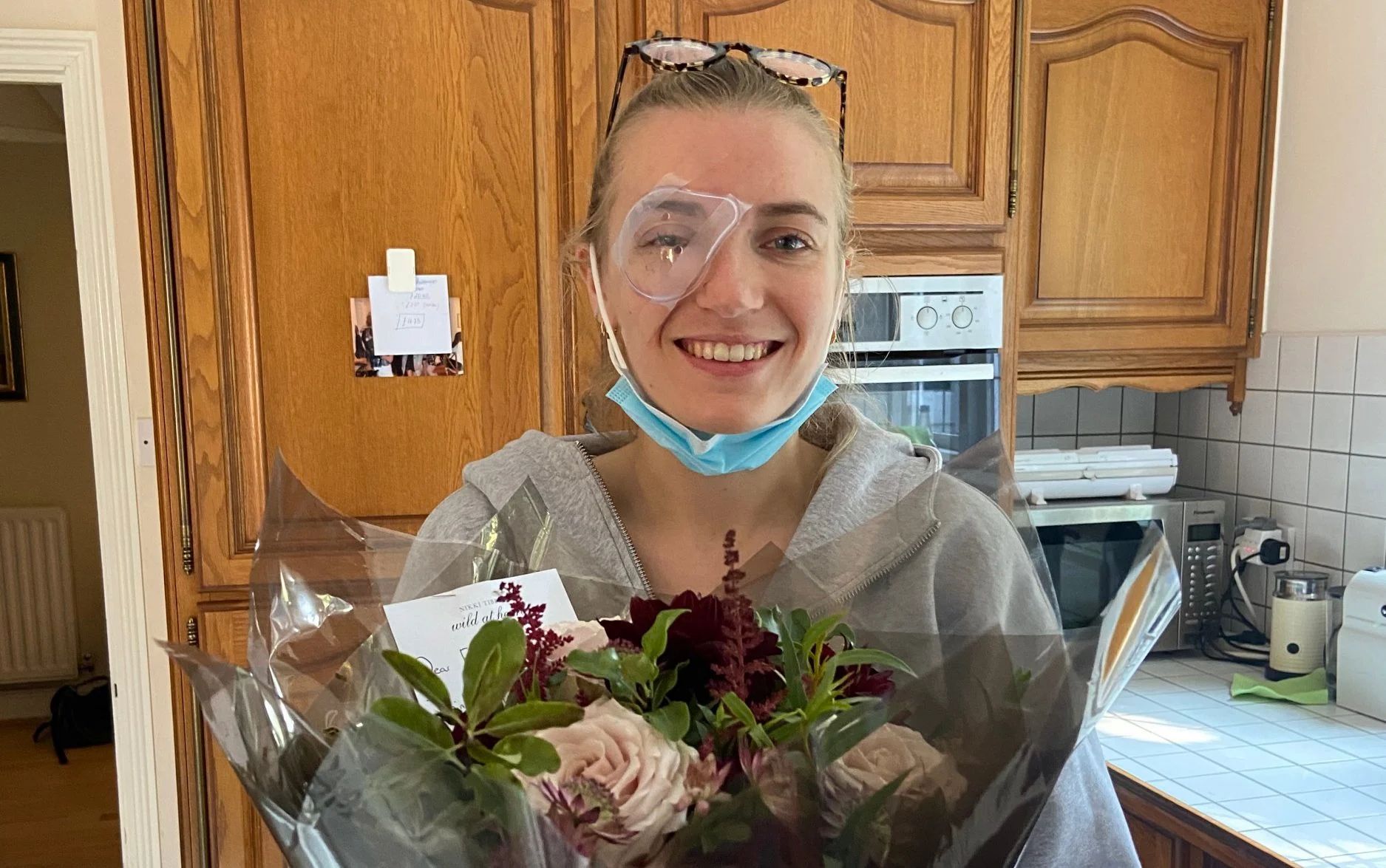 Ellie smiling and holding flowers with a bandage on her eye.
